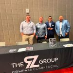 Four men standing in front of a table with their logo on a table banner.