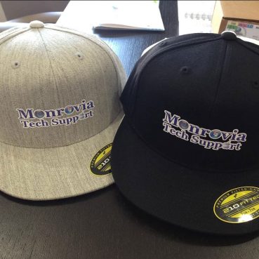 Gray and black baseball caps with Monrovia Tech Support logo on front.